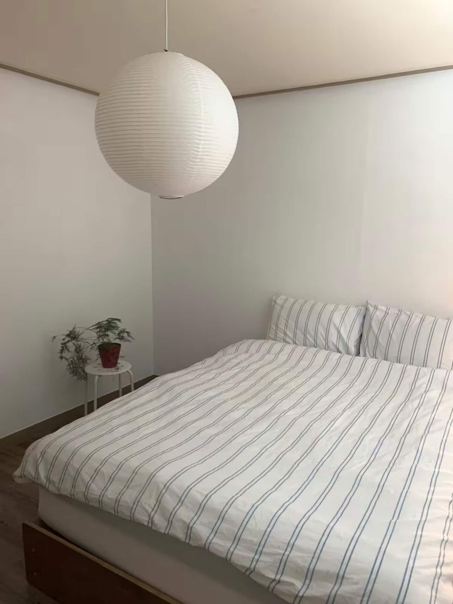 Queen bedroom with striped white bedding and a round pendant light