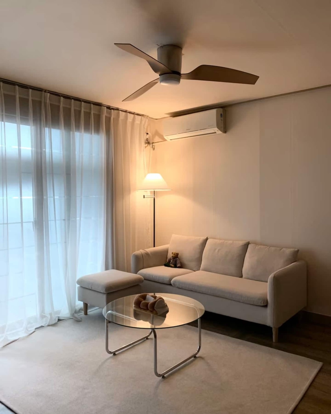 The actual living room with a ceiling fan, warm lighting and a cream sofa